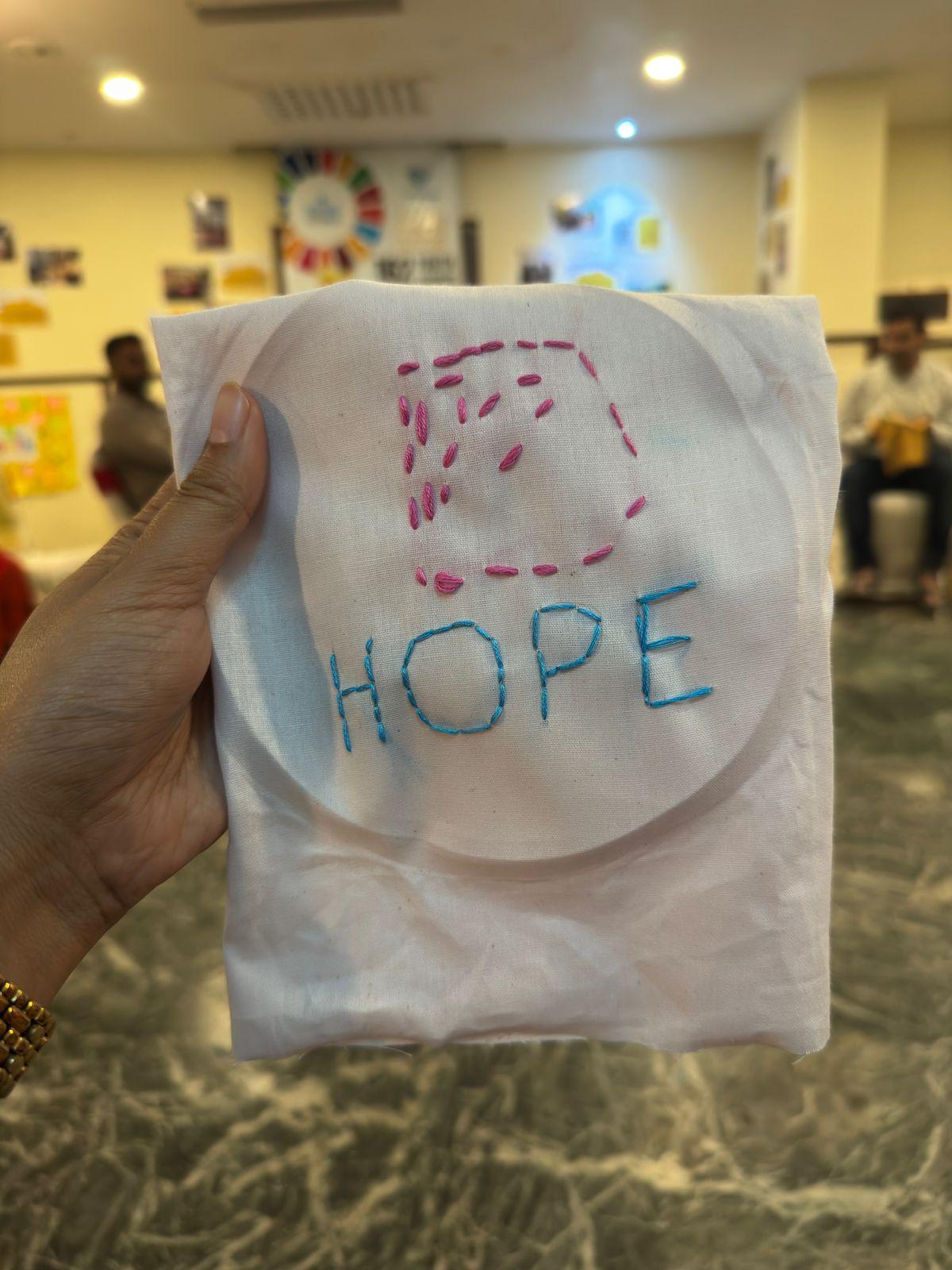 A hand holding a cloth embroidered with the word HOPE, made in a workshop